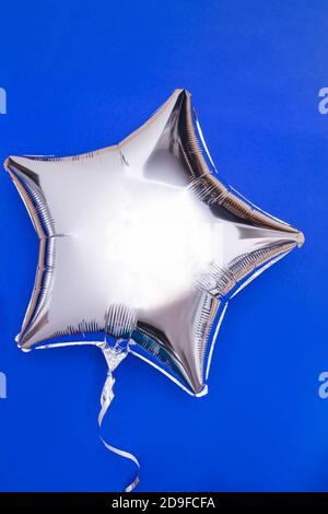 A silver glitter foil star shaped balloon isolated on blue Stock Photo