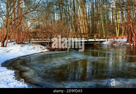Wooden bridge over the frozen Malenter Au (small river in Holstein Switzerland). Stock Photo