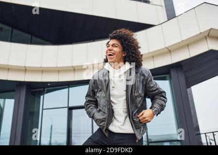 Handsome young man with curly black hair posing for the camera on the street against building Stock Photo