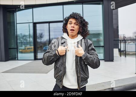 Handsome young man with curly black hair posing for the camera on the street against building Stock Photo