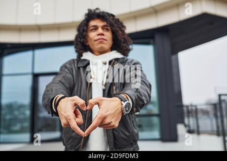 Handsome young man with curly black hair posing for the camera on the street against building Stock Photo