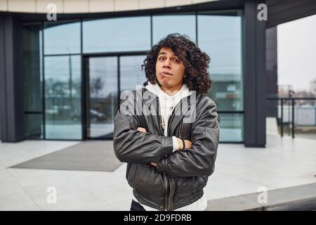 Handsome young man with curly black hair is on the street against building Stock Photo