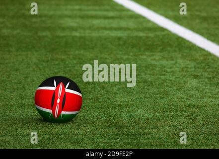 Kenya flag on ball at soccer field background. National football theme on green grass. Sports competition concept. Stock Photo