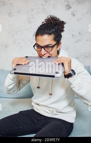 Angry young man with curly black hair goes crazy and angry with laptop in hands Stock Photo
