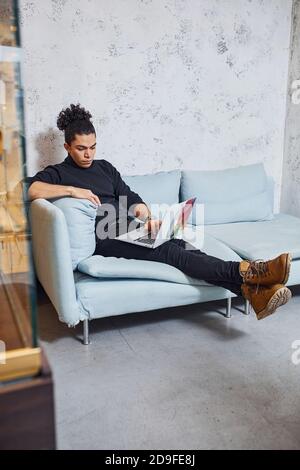 Handsome young man with curly black hair indoors with laptop Stock Photo