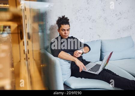 Handsome young man with curly black hair indoors with laptop Stock Photo