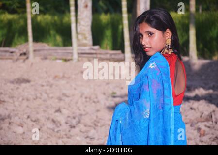 Close up of side face of an Indian teenage girl wearing blue sari with red blouse nose pin big earring standing on a plowed field, selective focusing Stock Photo