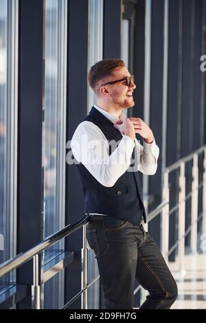 Man in elegant clothes and sunglasses is standing indoors and posing for the camera Stock Photo
