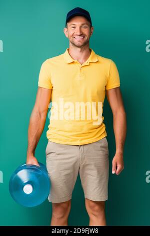 happy delivery man in cap carrying bottle of water on blue Stock Photo