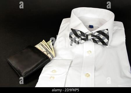 Folded white dress shirt with black and white plaid bow tie and leather wallet on black background Stock Photo