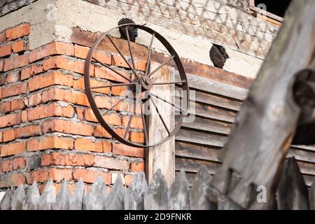 an old metal cart wheel stands by the fence Stock Photo