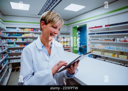 Caucasian pharmacist scrolling on digital tablet standing by medication counter in pharmacy  Stock Photo