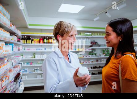 Caucasian senior pharmacist assisting mixed race patient giving advice on dosage intake while standing in pharmacy  Stock Photo