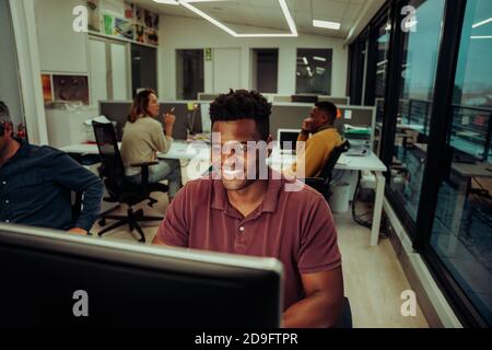 Happy businessman working late hours submitting assignments for the week sitting with colleagues in quiet office  Stock Photo