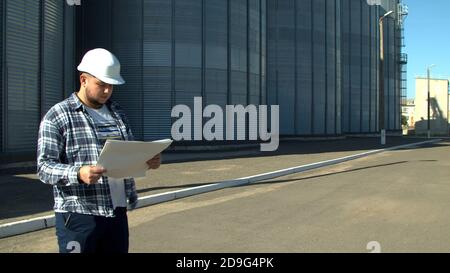 Professional engineer with blueprints inspecting agricultural silos Stock Photo