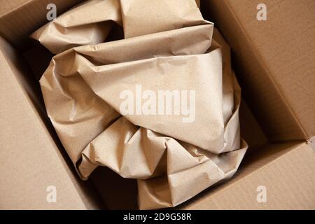 Crumpled wrapping craft brown paper in open after delivery paperboard box. Horizontal. Delivery, ecology, plastic free, resource overrun concept. Flat Stock Photo