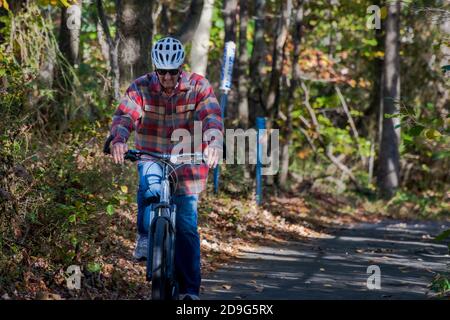 Reston, VA. USA -- November 4, 2020. Autumn photo of a man riding a bicycle on a path through dense foliage in Reston, VA. Stock Photo