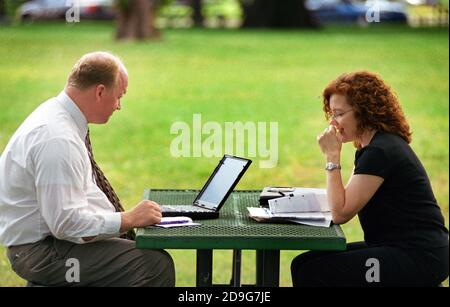 Business man on laptop works with secretary at picnic table in a public park Stock Photo