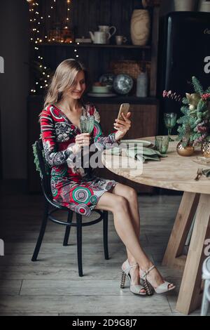 Beautiful woman with drink video calling. New Year with friend on smartphone. Stock Photo