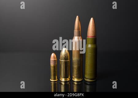 A row of bullets from small to large. Left to right .22 9mm .223 7.62x39. Weapon ammunition on a dark background. Stock Photo