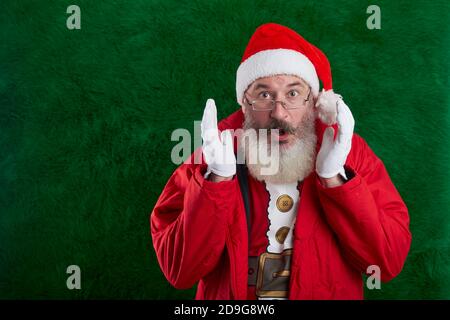 Mature bearded man with eyeglasses on face wearing Santa hat, Santa surprised and looks at camera, copy space Stock Photo