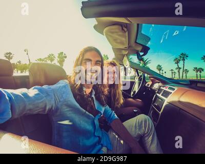 Happy young couple having fun during road trip in convertible car. Romantic lovers enjoying time together driving cabriolet auto in luxury vacation in Stock Photo