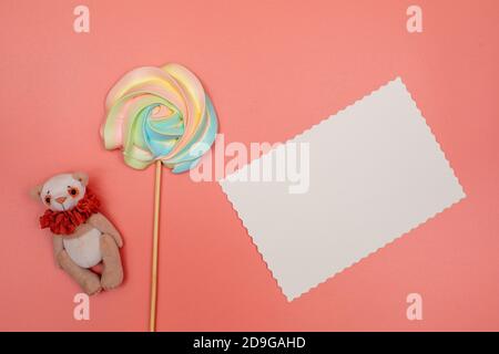 Blank white postcard, rainbow meringue on a stick and teddy bear on a pink background. Christmas, New Year, Valentine's Day, International Women's Day Stock Photo