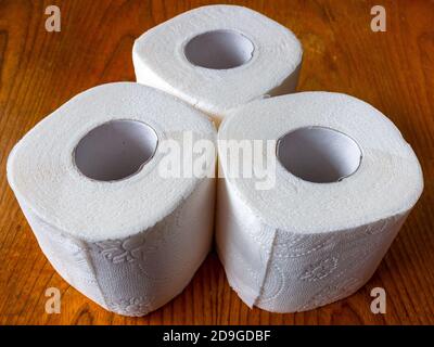 3 rolls of toilet paper stands in the shape of a triangle on a brown wooden table Stock Photo