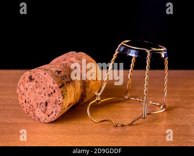 Cork plug with muselet(wire cage) from champagne or sparkling wine lies on a wooden surface with black background Stock Photo