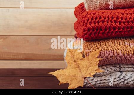 Stack of warm knitted sweaters. Autumn concept. Woolen jumpers and maple leaf on wooden background. Stock Photo