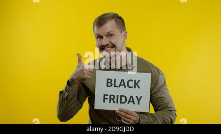 Cheerful handsome man smiling and showing Black Friday inscription, rejoicing good discounts, low prices for online shopping sales. Studio shot on yellow background Stock Photo