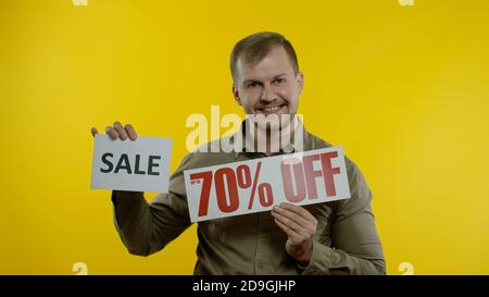 Great discounts. Happy joyful blonde man showing Sale word and showing Up To 70 percent Off purchase inscription. Shopping with low prices, Black Friday concept. Yellow background Stock Photo
