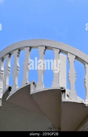 Upward perspective view of an exterior white stone spiral staircase against a clear blue sky background.