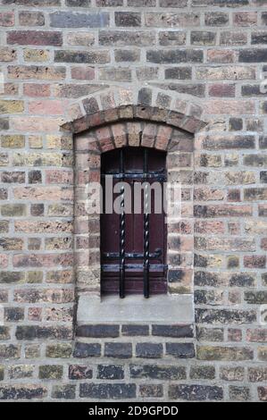 Close up view of a small wooden shuttered window, fortified with wrought iron black metal bars, in a brick wall. Stock Photo