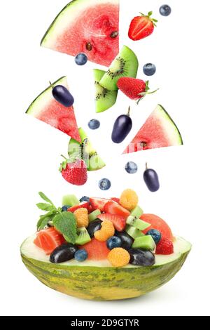 Delicious fruit salad in melon bowl with flying ingredients on white background Stock Photo