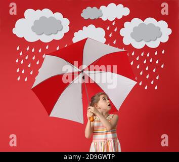 Surprised little girl holding umbrella under drawn cloudy sky with rain drops on color background Stock Photo
