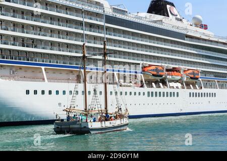 An old-fashioned sailing vessel passing by the side of a huge ocean liner. The scow 'Ted Ashby' and the cruise ship 'Viking Orion', Auckland, NZ Stock Photo