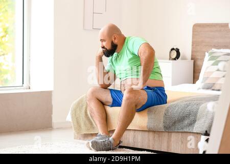 Sad overweight man sitting on bed at home. Weight loss concept Stock Photo