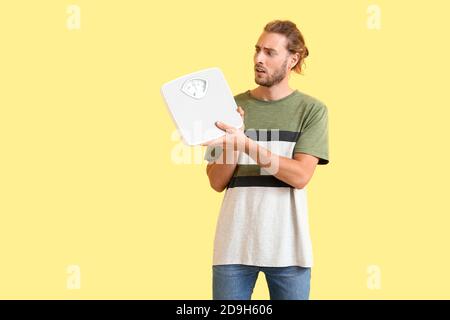 Man with sudden weight loss problem holding measuring scales on color background. Diabetes symptoms Stock Photo