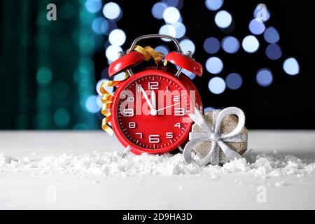 Christmas gift and alarm clock on table against blurred lights Stock Photo