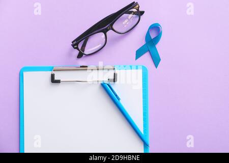 Blue ribbon, eyeglasses and clipboard on color background. Prostate cancer awareness concept Stock Photo