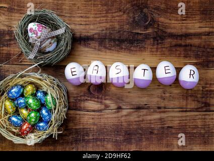 Top view of colorful eggs spelling "EASTER" on a wooden table with candies on it Stock Photo