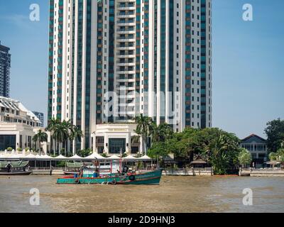 The Peninsula Hotel on the bank of the Chayo Phraya River in Bangkok, with a tug boat in the foreground. Stock Photo