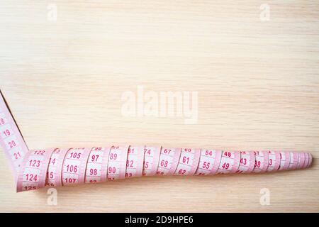 top view of curly measuring tape on a beige wooden background, copy space Stock Photo