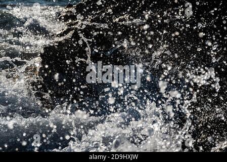 Detail of a wave breaking on the shore against a rock, splashing many drops of water. Fast shutter frozen motion. Stock Photo