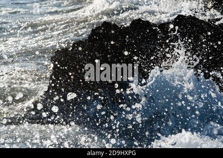 Detail of a wave breaking on the shore against a rock, splashing many drops of water. Fast shutter frozen motion. Stock Photo