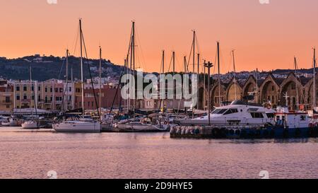 Sunrise over Old Venetian harbour of Chania, Crete, Greece. Sailing boats anchored by pier, Old Venetian shipyards or Neoria and Cretan mountains