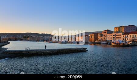 Sunrise at Old Venetian harbour of Chania, Crete, Greece. Unrecognizable male and his bicycle standing on pier and enjoying the view. Stock Photo