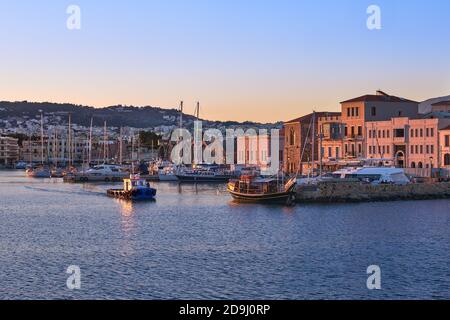 Fishing boat leaving Old Venetian port of Chania, Crete, Greece at sunrise. Sailboats, yachts, Grand Arsenal, Old Venetian shipyards or Neoria  Stock Photo