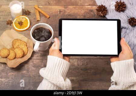 mockup image of woman's hands holding black tablet pc with white blank screen, coffee cup on wooden rustic table. winter Christmas time Stock Photo